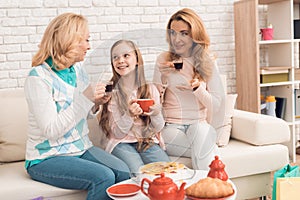 Mom, grandmother and little girl are drinking tea together, sitting at the table.