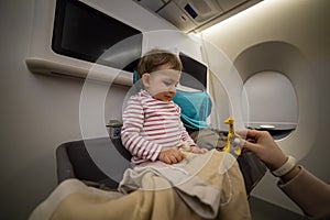 Mom hand plays a toy with a happy smiling little cute toddler sitting in the baby bassinet of an airplane. close-up