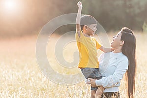 Mom is happily carrying her son in the meadow. Asian young mother and her little child at sunset. Soft focus