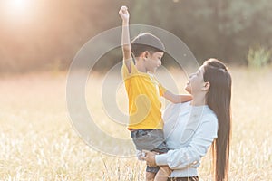 Mom is happily carrying her son in the meadow. Asian young mother and her little child at sunset. Soft focus