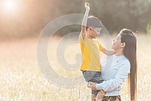 Mom is happily carrying her son in the meadow. Asian young mother and her little child at sunset. Soft focus