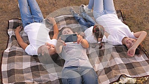 Mom and happy children are photographed on smartphone in park. Mother and daughters take a selfie while traveling, lying