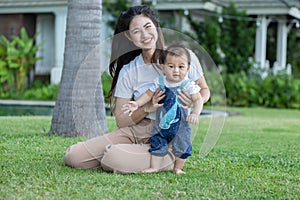 Mom helping and support baby learn to walk with love outdoors on grass. First steps of baby learning walk with family. Adorable