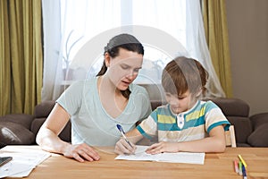 Mom helps child boy do lessons at home.