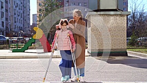 mom helps daughter learn to walk on crutches. plaster on your feet.