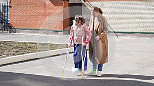 mom helps daughter learn to walk on crutches. plaster on your feet.