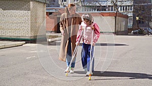 mom helps daughter learn to walk on crutches. plaster on your feet.