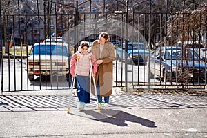 mom helps daughter learn to walk on crutches. plaster on your feet.