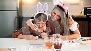 Mom helps her daughter color eggs for Easter. Family in hair holders bunny ears