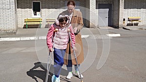 mom helps her daughter learn to walk on crutches.