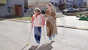 mom helps her daughter learn to walk on crutches.