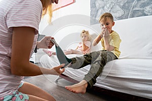 Mom helps the little boy take off his socks and lightly tickles his feet. The boy giggles