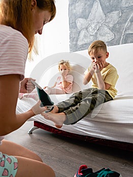 Mom helps the little boy take off his socks and lightly tickles his feet. The boy giggles