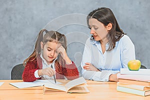 Mom helps me do my daughter`s homework. During this they are sitting on a gray background.