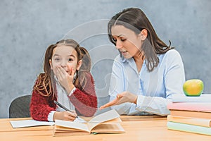 Mom helps me do my daughter`s homework. During this they are sitting on a gray background. A schoolgirl closed her mouth