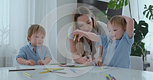 Mom helps two sons of 2 and 4 years old to do preschool homework to draw a picture with pencils