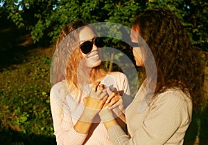 Mom and her adult daughter hold hands in a summer park, happy women wearing sunglasses