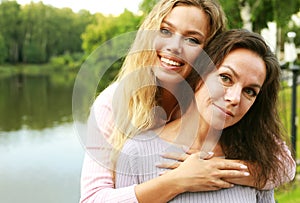 Mom and her adult daughter are hugging in the park near the lake, happy family