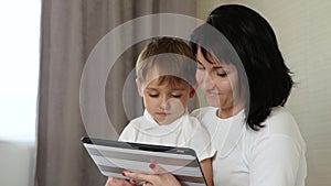 Mom and her child spend time at the tablet at home, playing and watching cartoons, playing video games, using