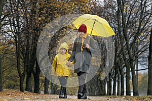 Mom and her child are walking in the park on rainy autumn day. Mom and son with big yellow umbrella
