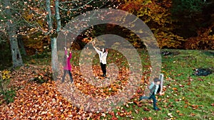Mom and her children have fun in the autumn forest. They jump and throw leaves into the air. They are laughing. The