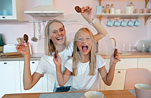 Mom with her daughter fooling around in the kitchen holding American chocolate chip cookies in her hands. dressed alike