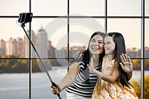 Mom and her daughter are making a common photo on smartphone using selfie stick.