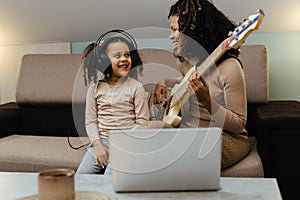 Mom with her daughter playing electric guitar together at home, happy family