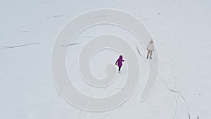 Mom and her little daughter are learning to skate on the rink. Winter time. Aerial view.