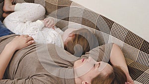 Mom and her little daughter are lying on the couch trying to sleep, mom is asleep and the child is playing and laughing