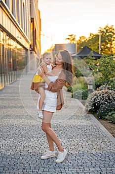 Mom and her little daughter playing on city street at sunset lights in summer
