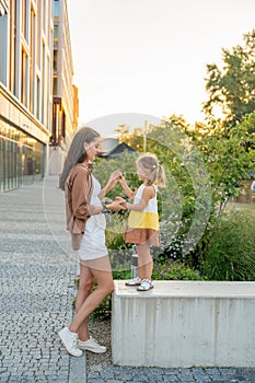 Mom and her little daughter playing on city street in sunset time