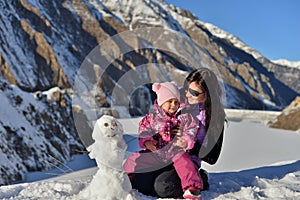 Mom and her little daughter in the winter sculpt a snowman in the mountains.