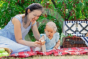 Mom and her newborn girl assemble a tower of wooden cubes at a picnic in the park. Mother and daughter for 10-12 months play
