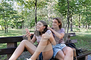 Mom and her teenage daughter have fun laughing on a walk in a summer park. Using a smartphone