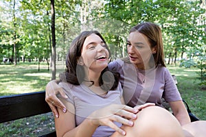 Mom and her teenage daughter have fun laughing on a walk in a summer park. Using a smartphone