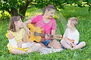 Mom with her two children play guitar at the park