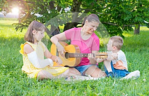 Mom with her two children play guitar at the park