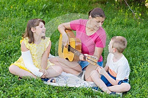 A mom with her two children play guitar at the park