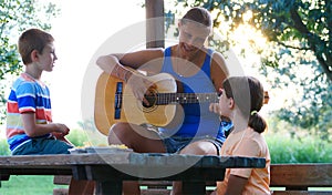 Mom and her two children sing songs together playing guitar outdoors on a sunny day. Concept of relaxation and healthy life