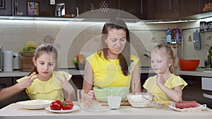 Mom and her two daughters have fun in the kitchen. Mom teaches kids how to make pizza. Happy mother and happy children