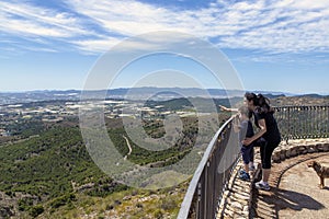 Mom with her young son on the railing of a lookout point, showing him the landscape in the distance with her finger