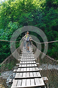 Mom and his son tourists cross the mountain river on suspension bridge