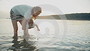 Mom holds the baby in her arms, the baby reaches for the water and splashes it.