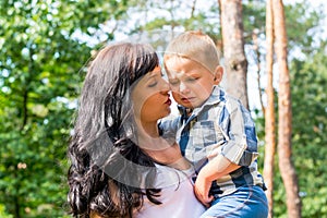 Mom holds in her arms and comforts her little boy who is crying, in the park