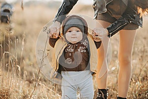 mom holds her baby boy by the hands for a walk. Baby's first steps