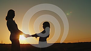 Mom holds her daughter`s hands, stand alone at sunset. Single parent concept