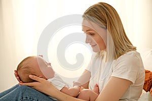 mom holds a newborn baby in her arms. in the background the sun shines from the window