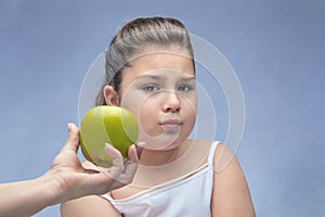 Mom holds out a green Apple to a fat kid. refusal of proper nutrition . parental control of nutrition. problem of obesity. blue