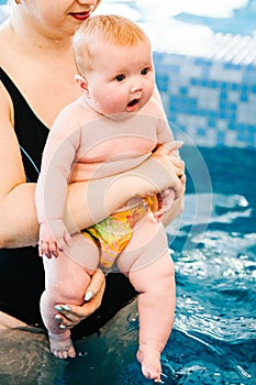 Mom holds surprised child and do exercises in water. Young mother, swimming instructor and happy little girl in pool. Teaches